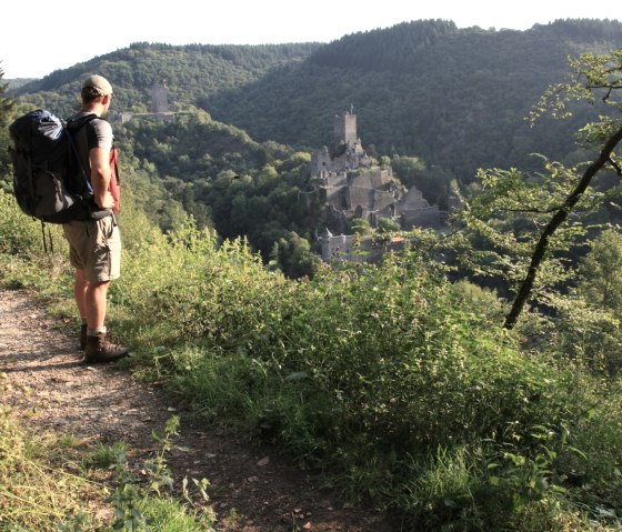 A hiker with a rucksack stands on a path and looks out over the Manderscheid castles in the green hilly landscape of the Eifel., © Björn Nehrhoff
